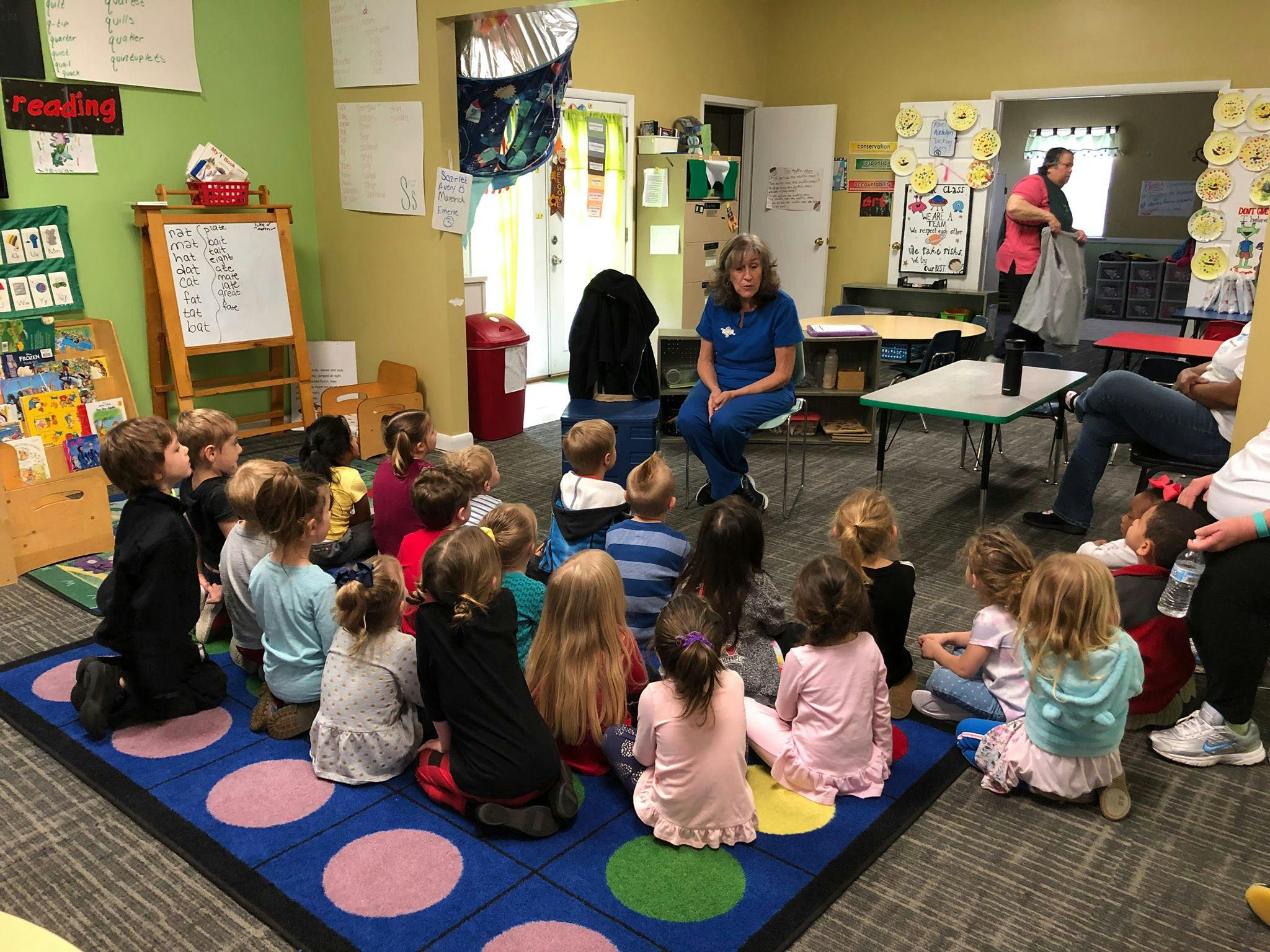 Adult speaking to a group of children sitting on a rug in a classroom