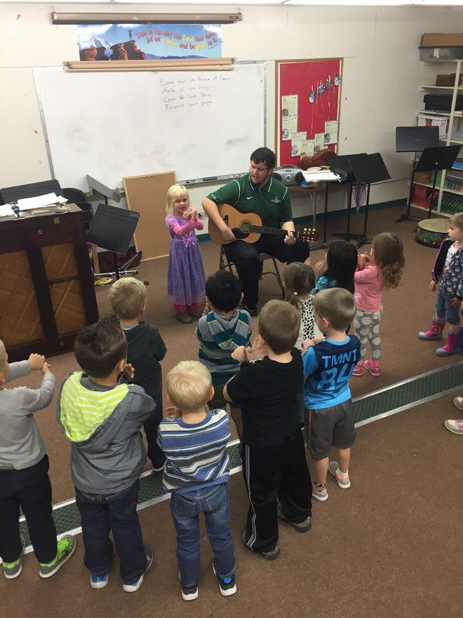 Adult playing guitar for a group of children in a classroom