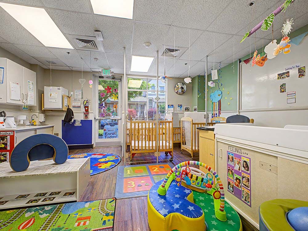 daycare classroom with multiple cribs, changing station, and play areas