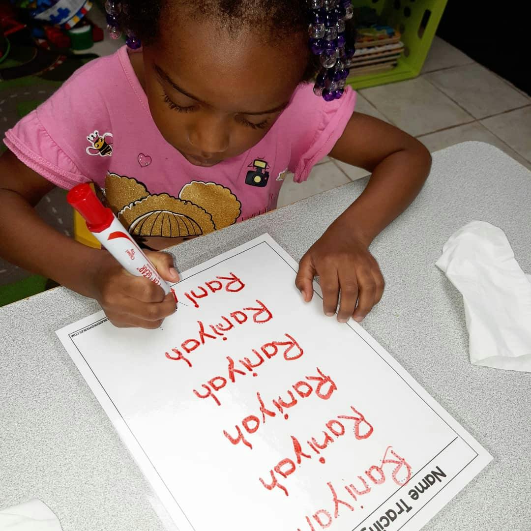 Child writing on a name tracing worksheet with a red marker
