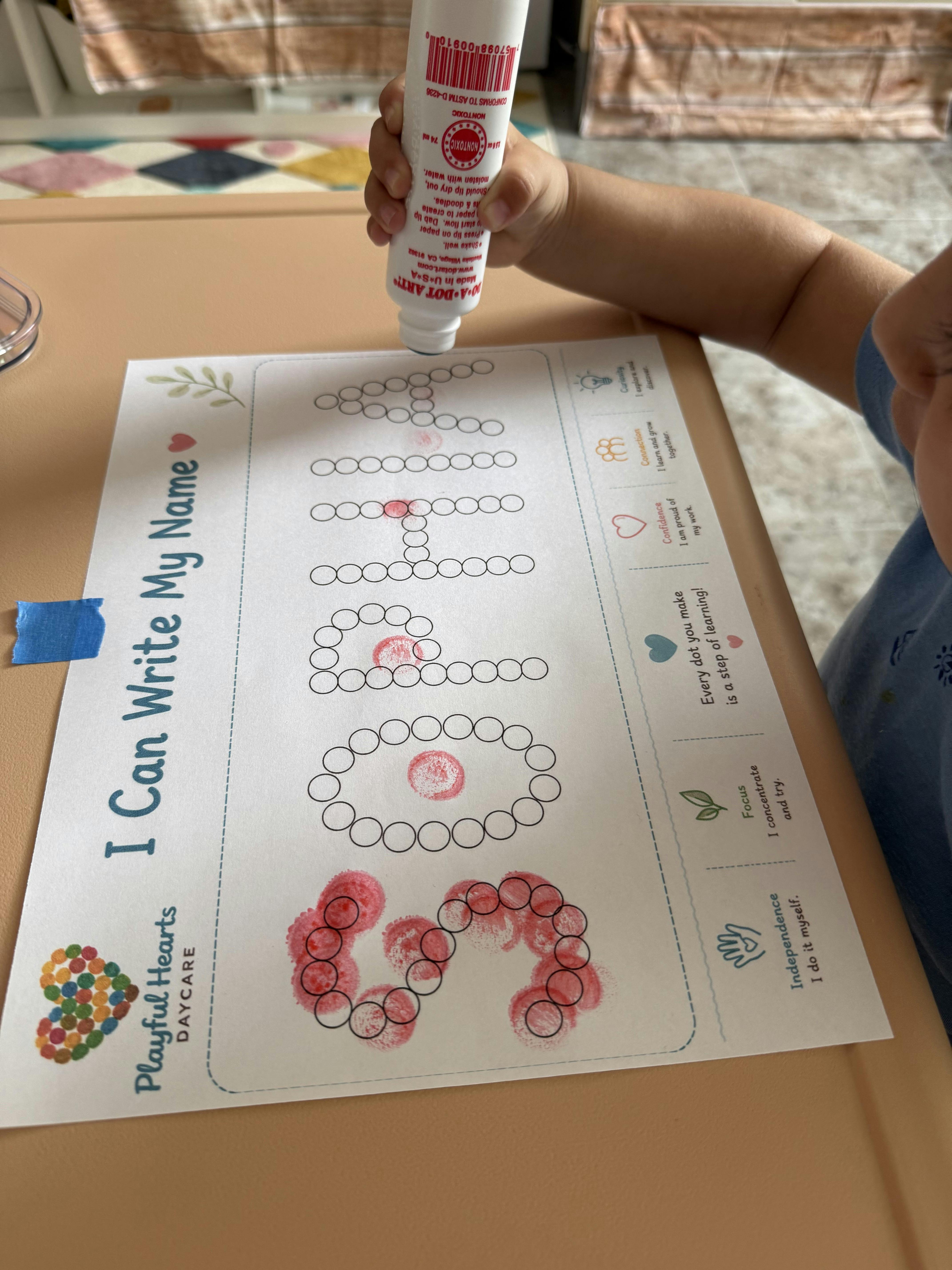Child using a dot marker on a name-writing worksheet