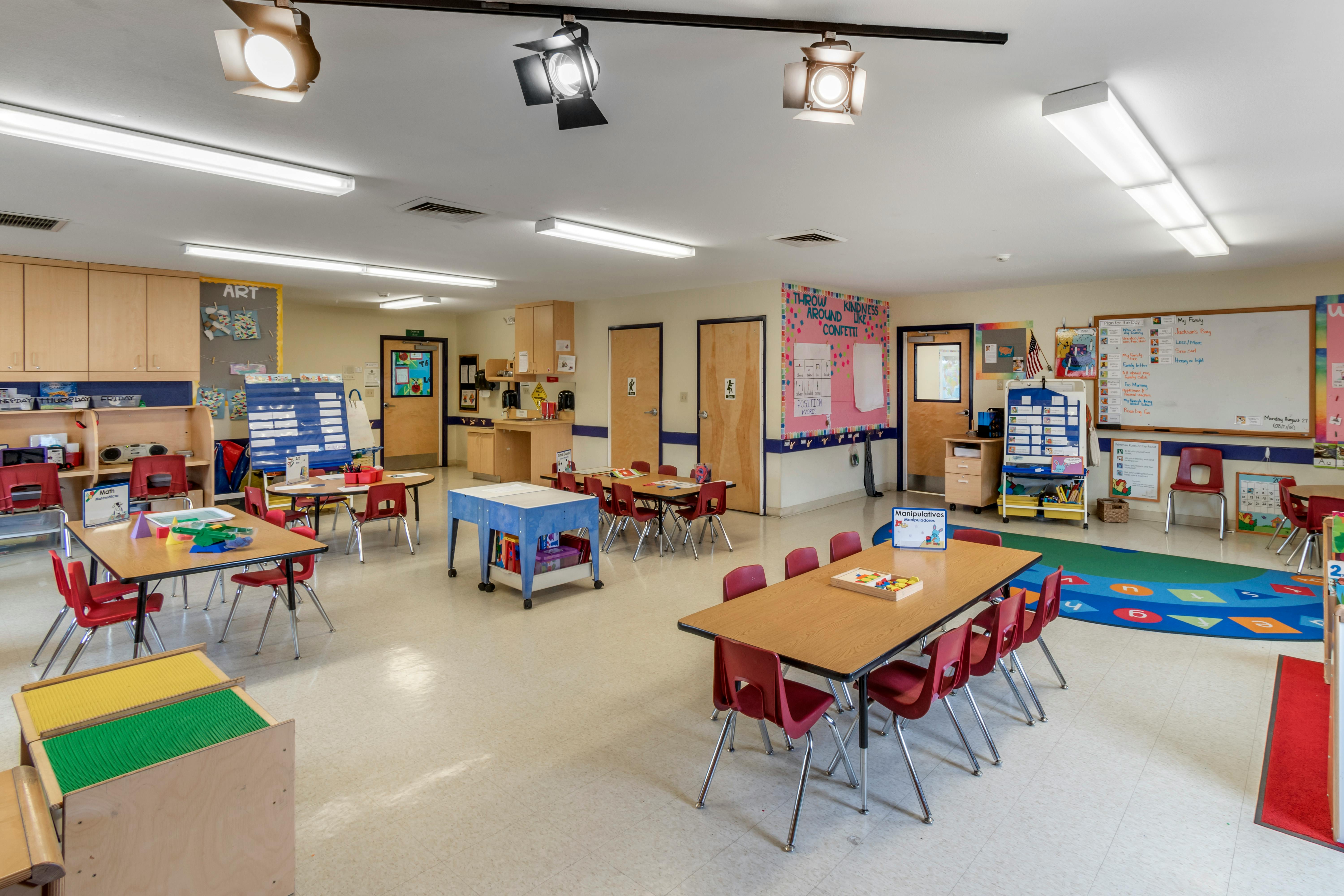 Empty classroom with small tables and red chairs, classroom decorations on walls