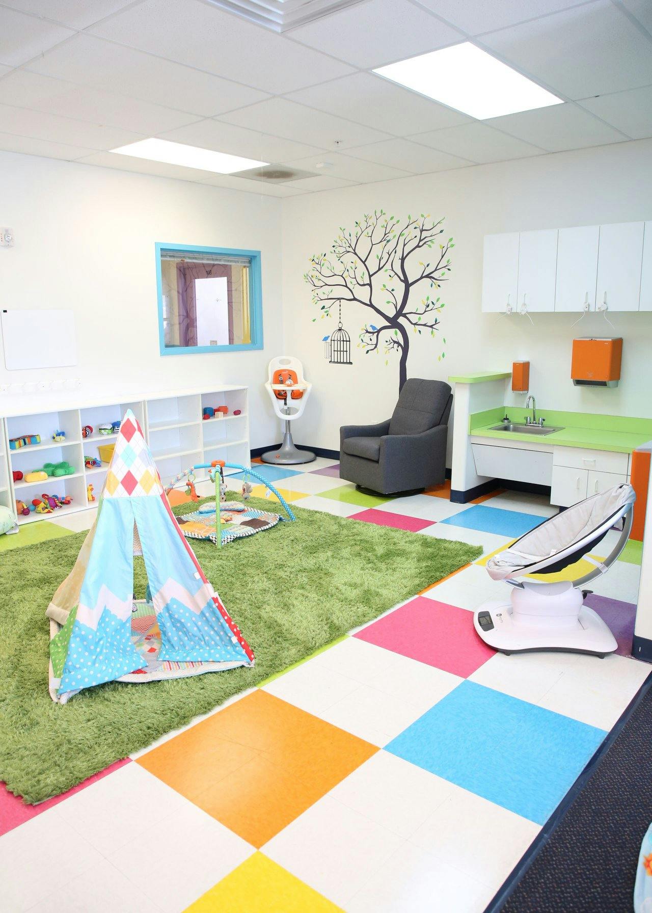 Playroom with colorful floor tiles, green rug, teepee, and baby equipment