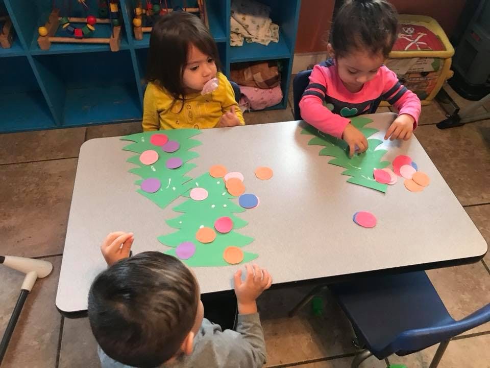 Three children at a table decorating green paper trees with colorful circles