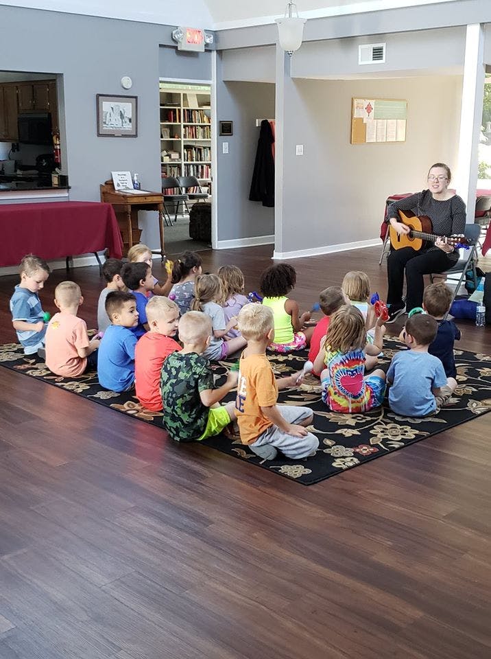 Adult playing guitar for a group of children sitting on a rug