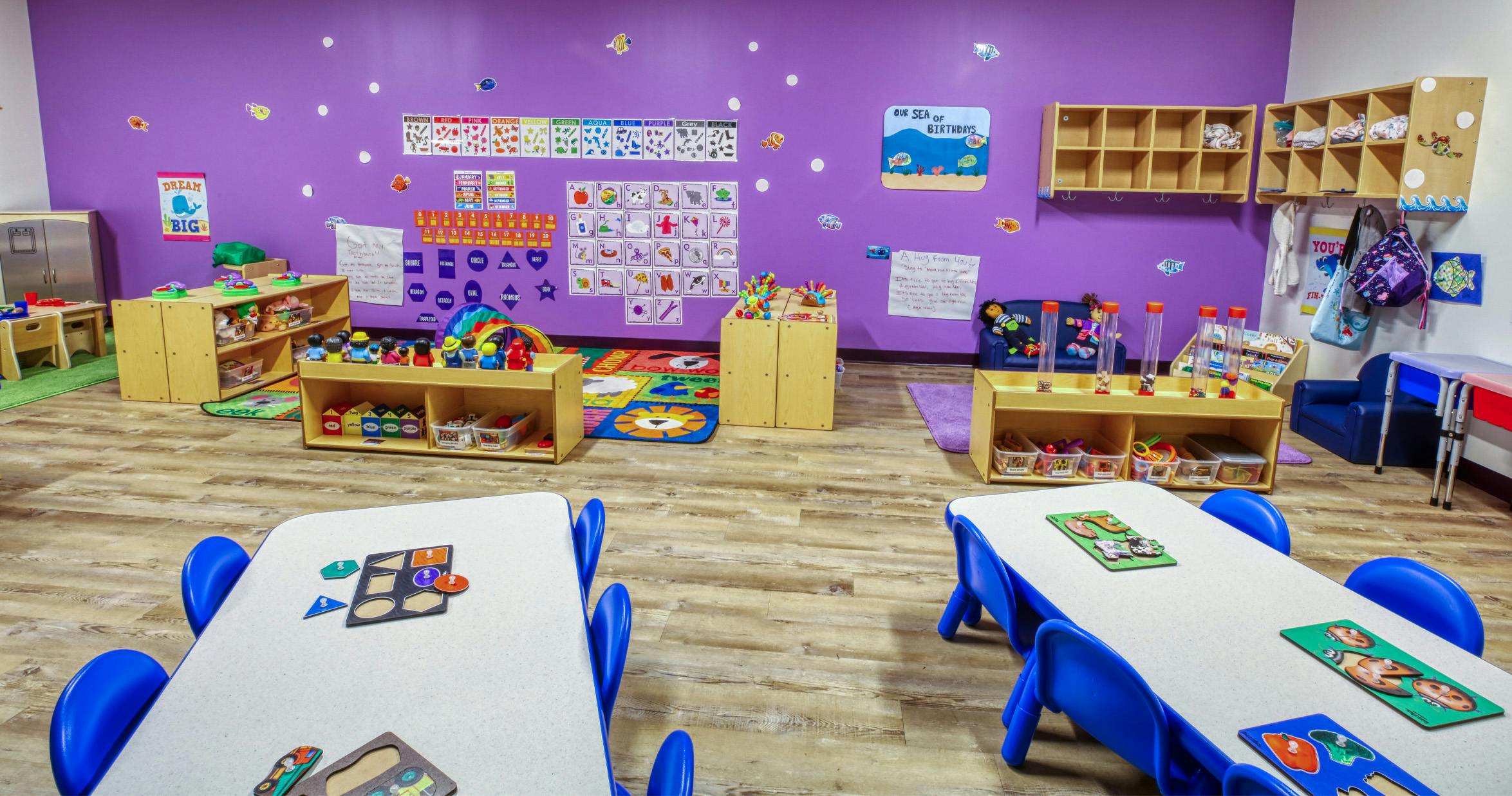 Classroom with purple walls, small tables, and shelves filled with toys