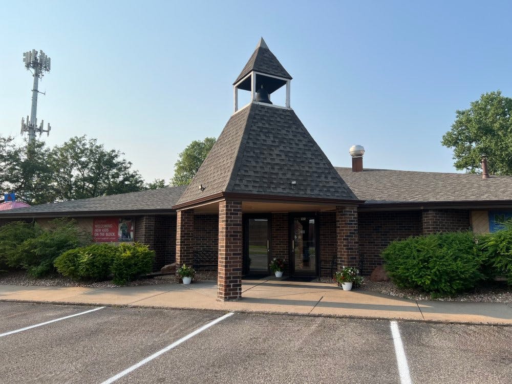 Brick building with a steep shingled roof and small bell tower above the entrance