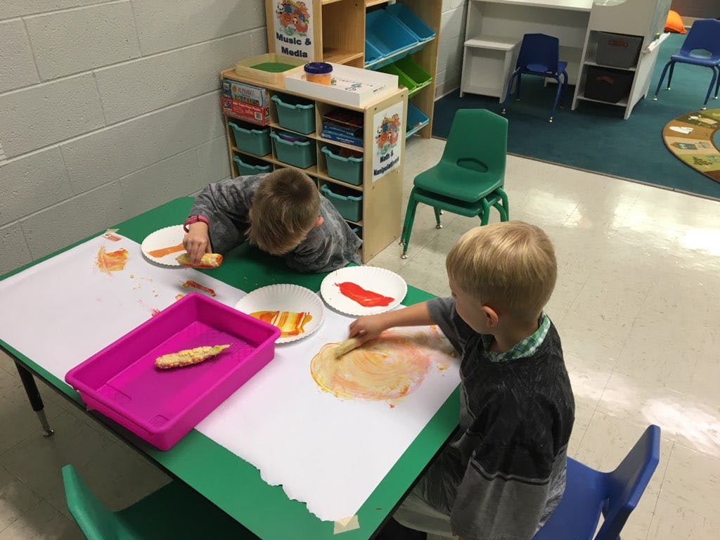 Two children painting at a table in a classroom