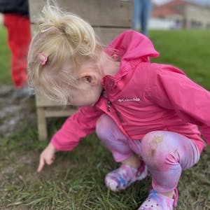 Child in pink jacket crouching and pointing at the ground