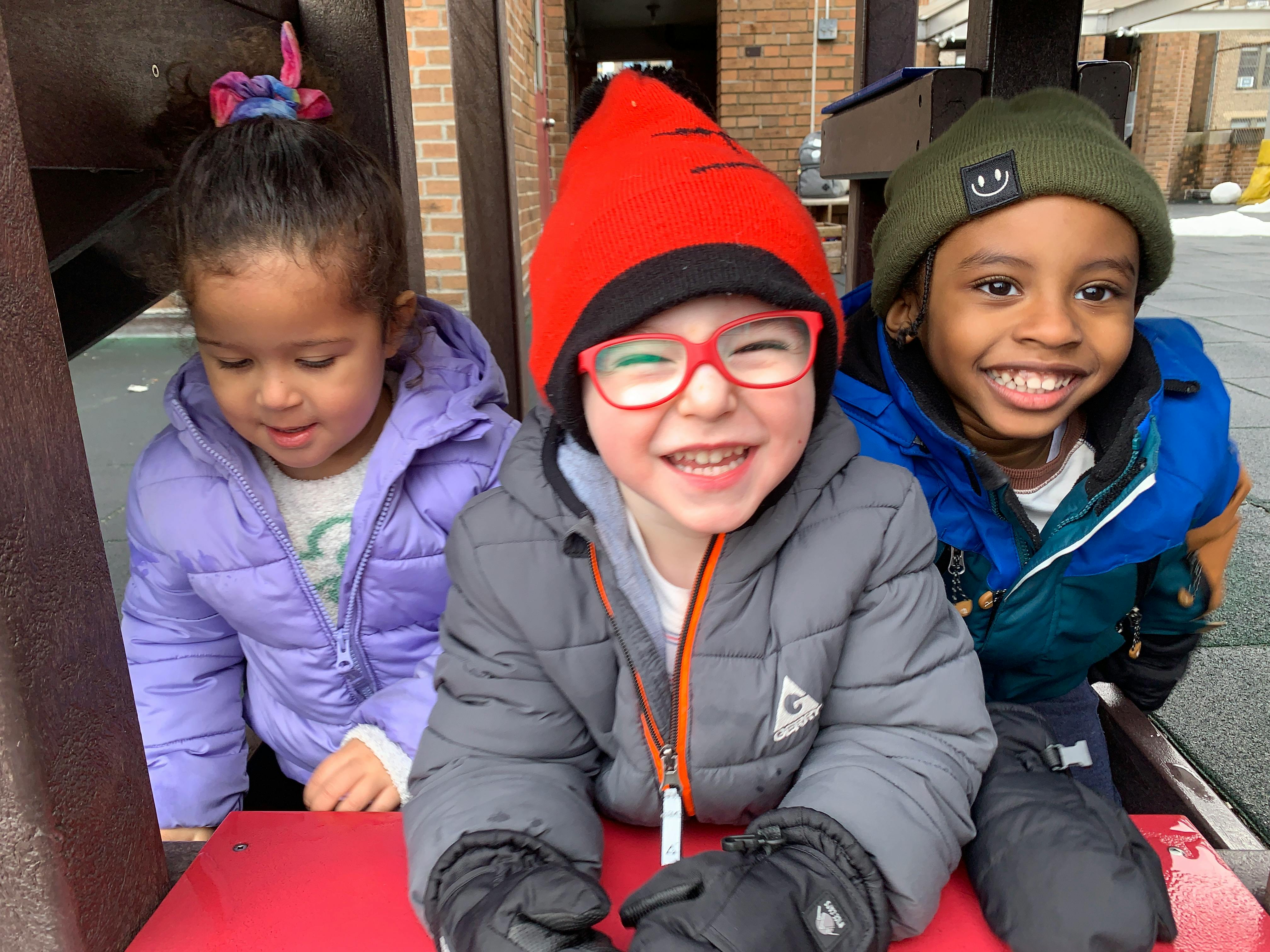 Three children bundled in winter coats and hats on a playground structure
