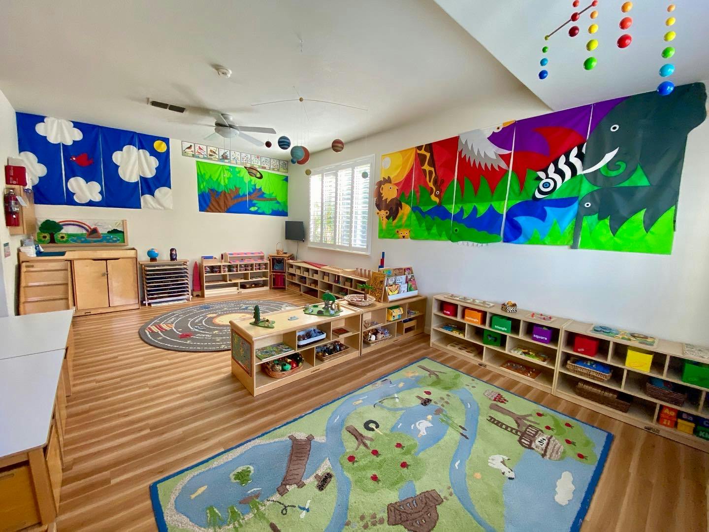 Classroom with colorful murals, rugs, and wooden shelves with learning materials
