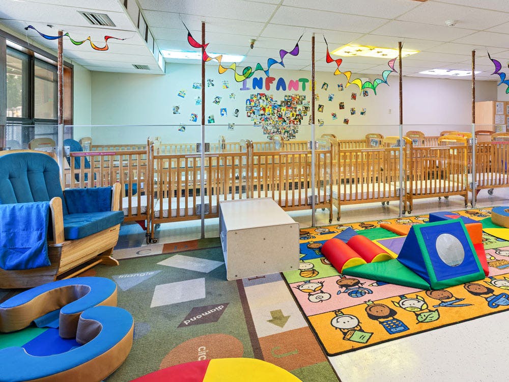 A classroom with several cribs and colorful play mats
