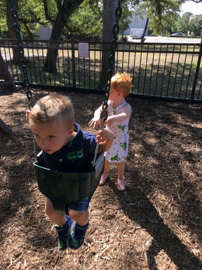 Two children on a playground, one in a swing and one standing