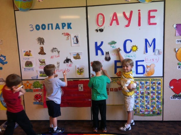 Three children interacting with a whiteboard covered in letters and animal pictures
