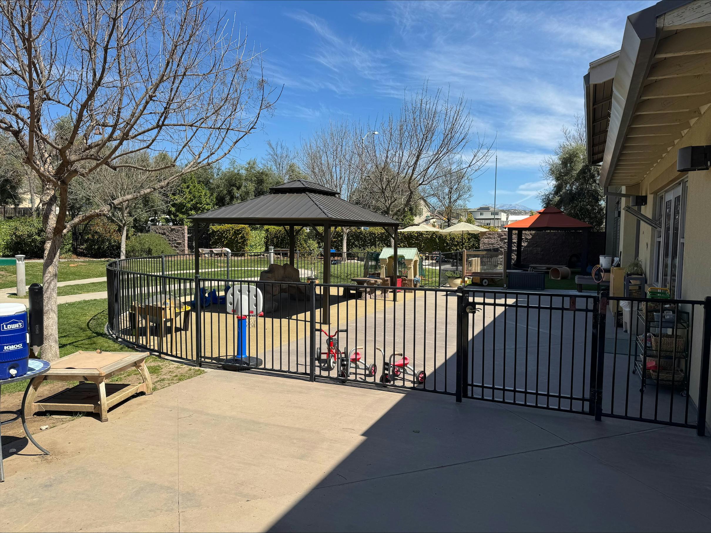 Outdoor playground area with a black fence, gazebo, and small basketball hoop