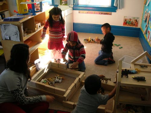 Adult and children playing with wooden blocks and toys in a classroom
