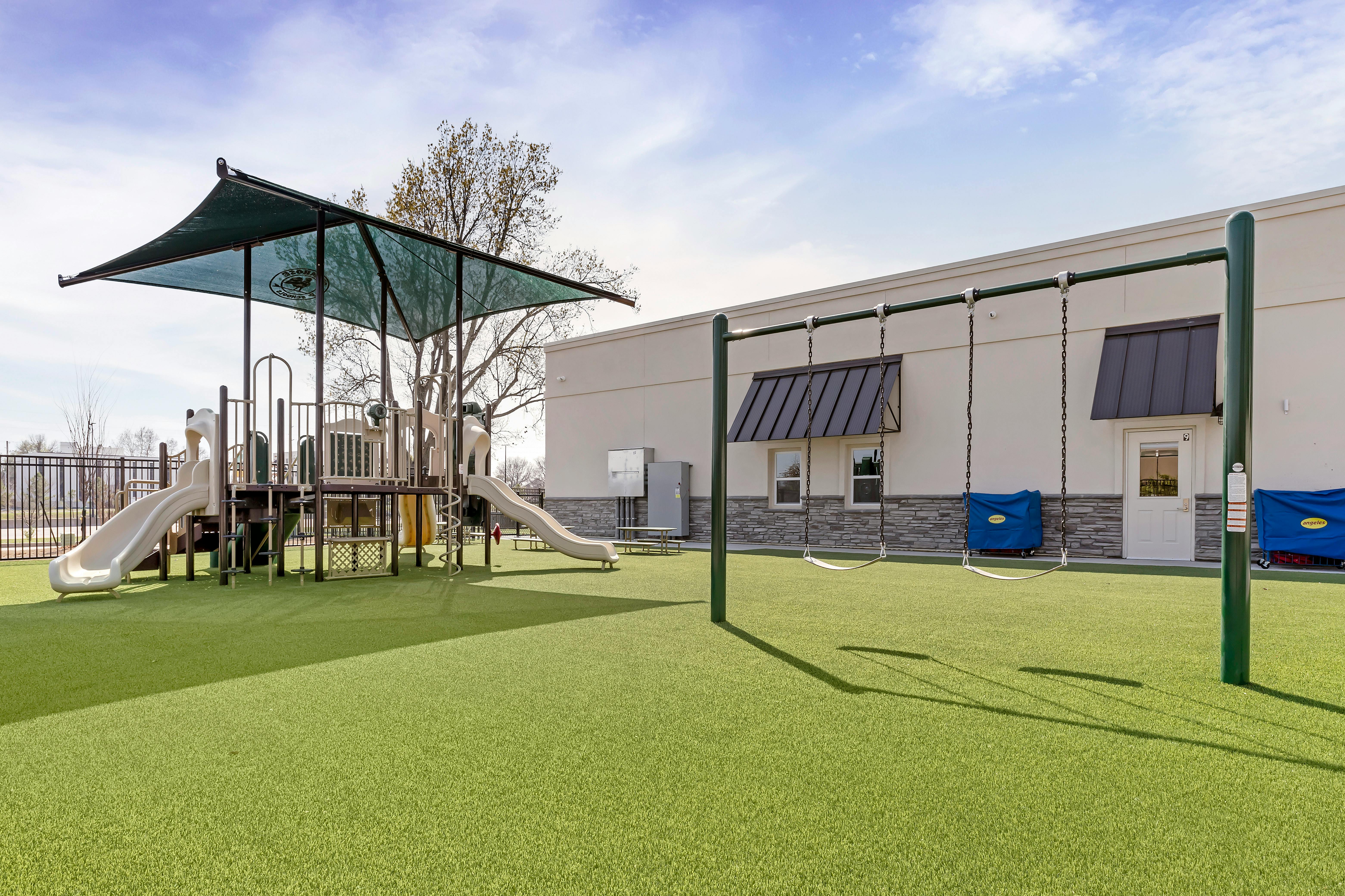 Outdoor playground with slides, climbing structure, and swings on artificial turf