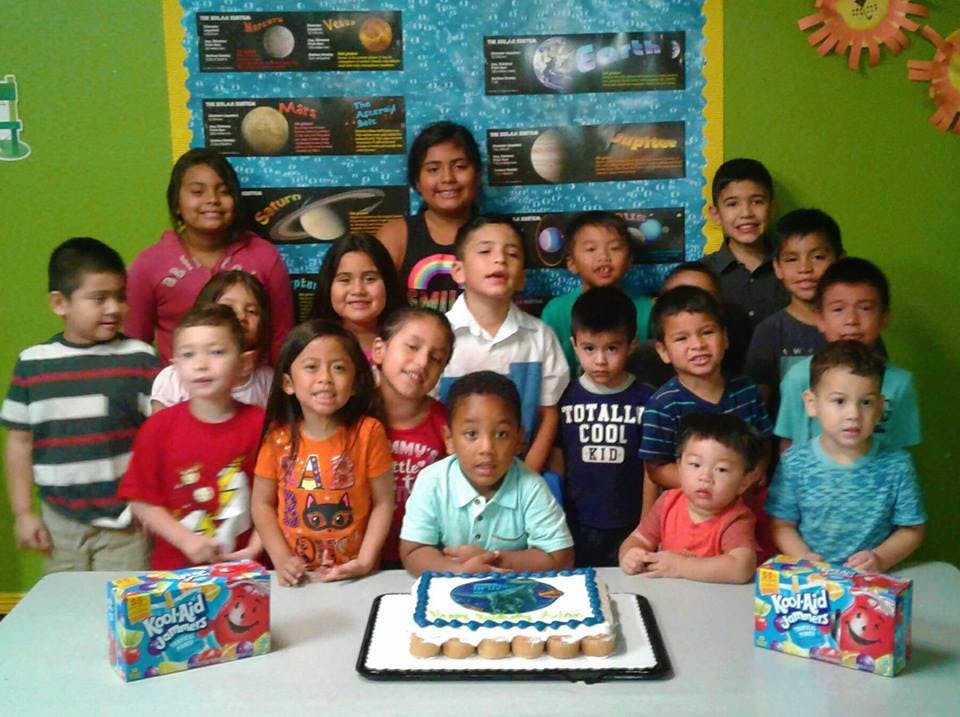 Group of children and adults posing with a cake on a table