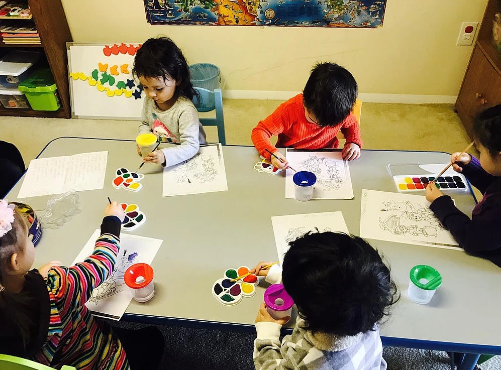 Children sitting at a table doing crafts and looking at crafts