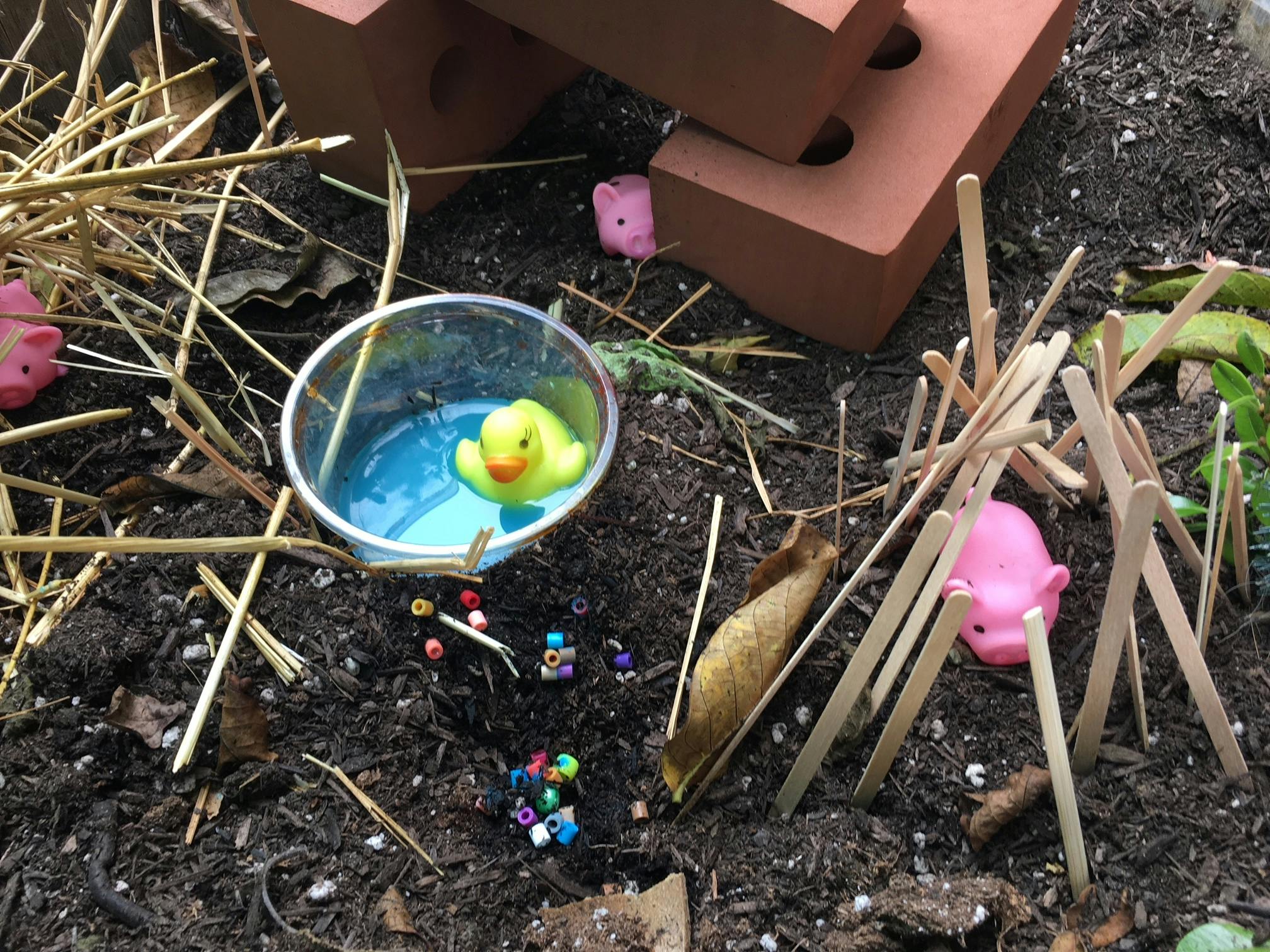 Rubber duck in a cup of water with sticks and beads on dirt