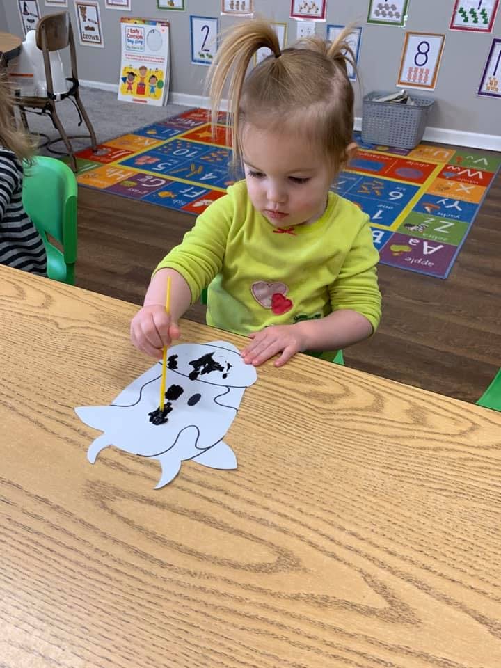 Child painting a paper cutout of a seal at a table