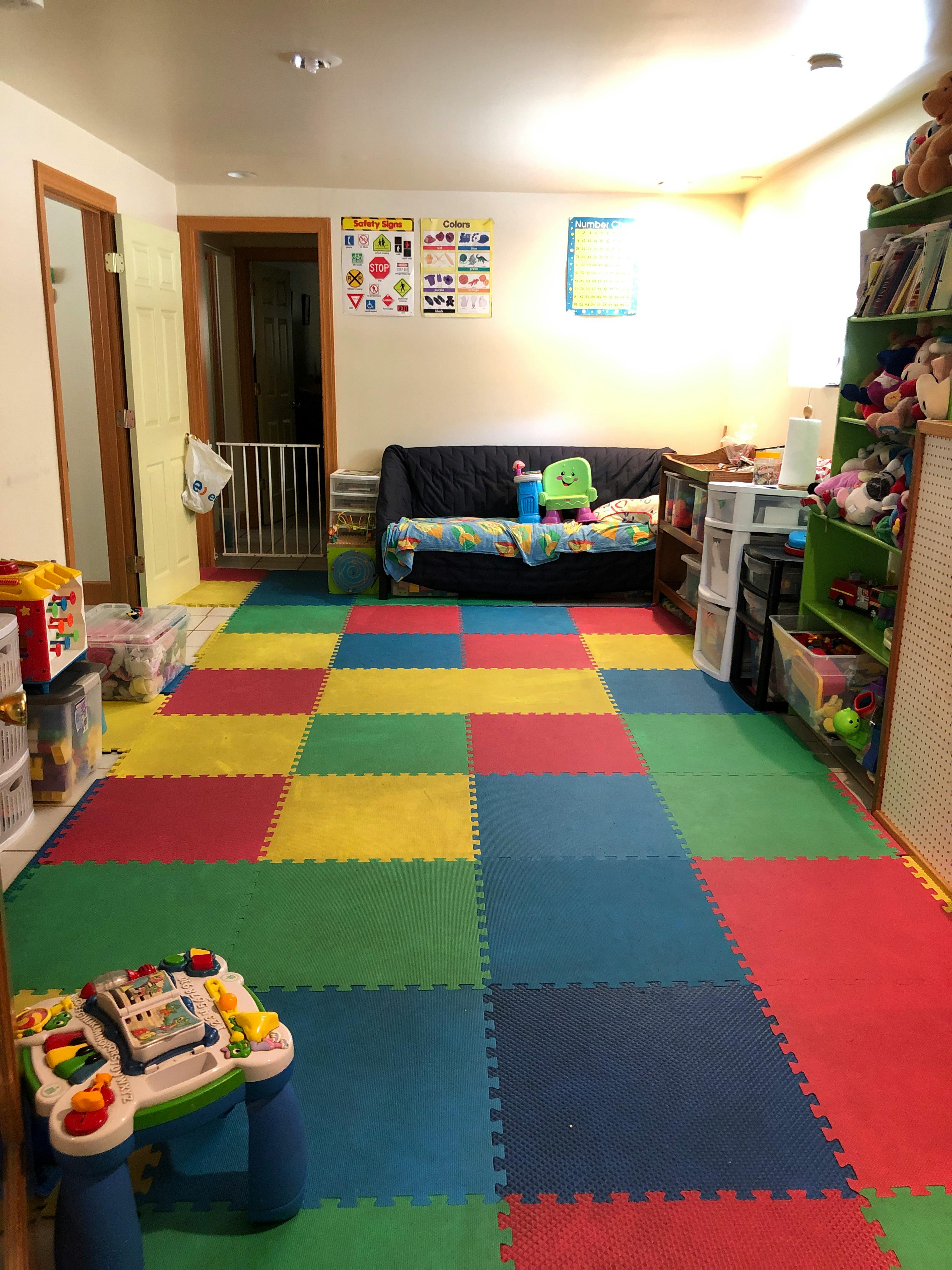 Playroom with colorful interlocking floor mats, sofa, and toy shelves