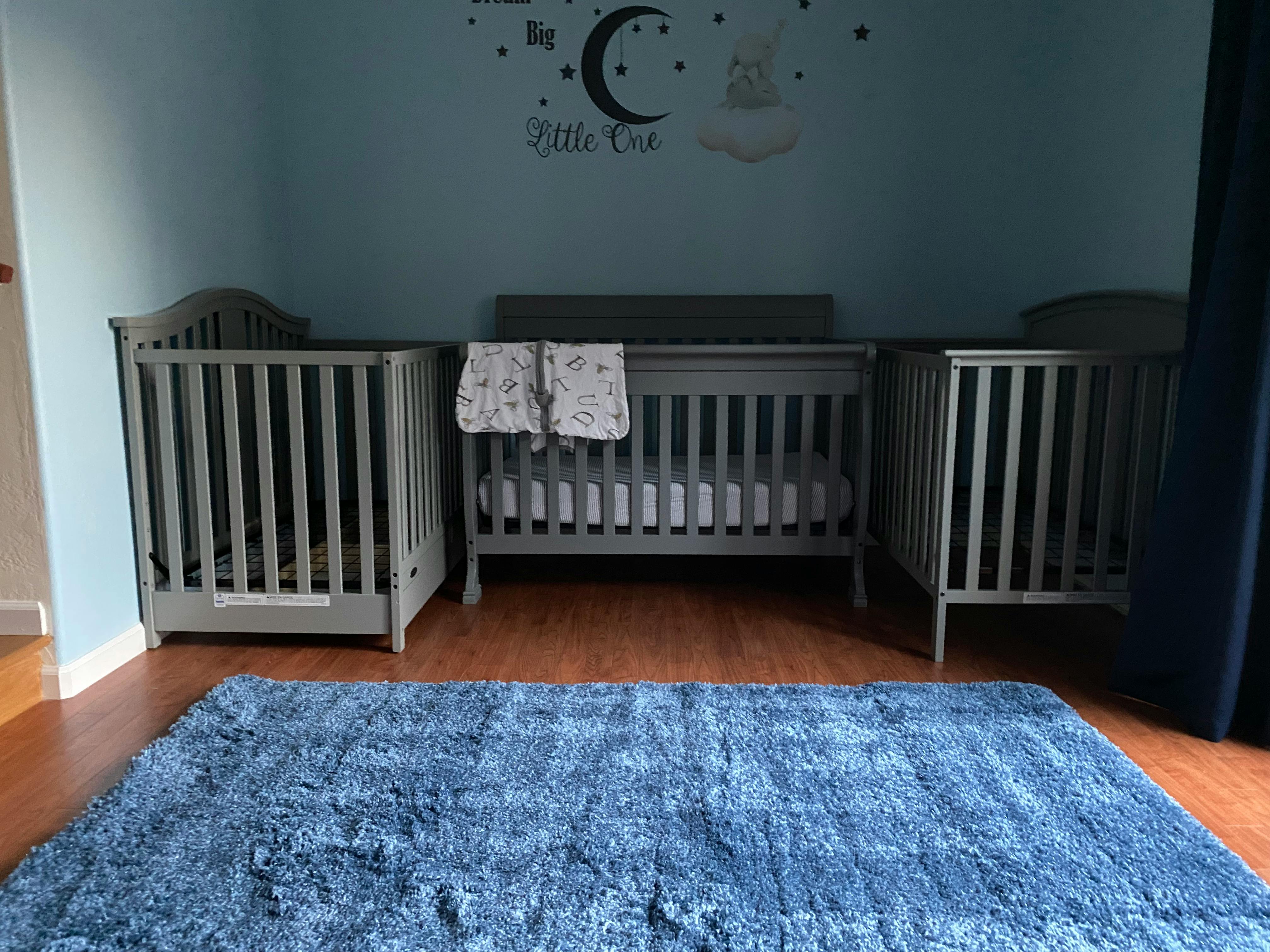 Three cribs in a nursery with a blue rug