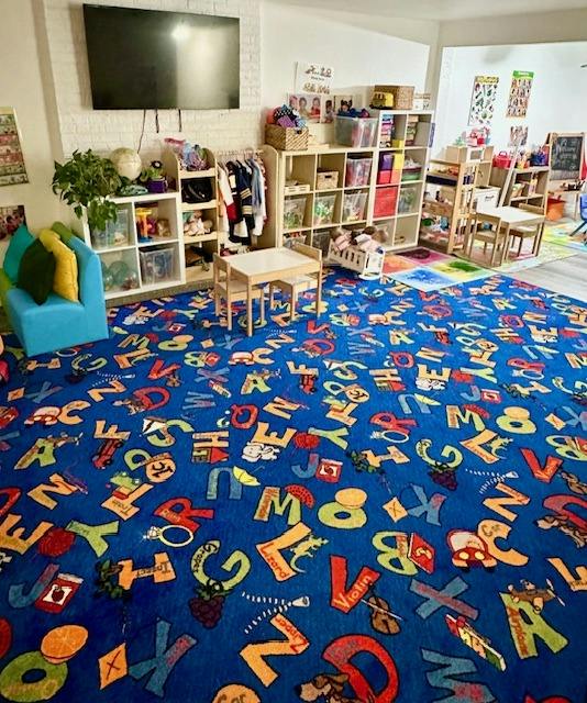 A children's playroom with an alphabet rug, small chairs, and storage units