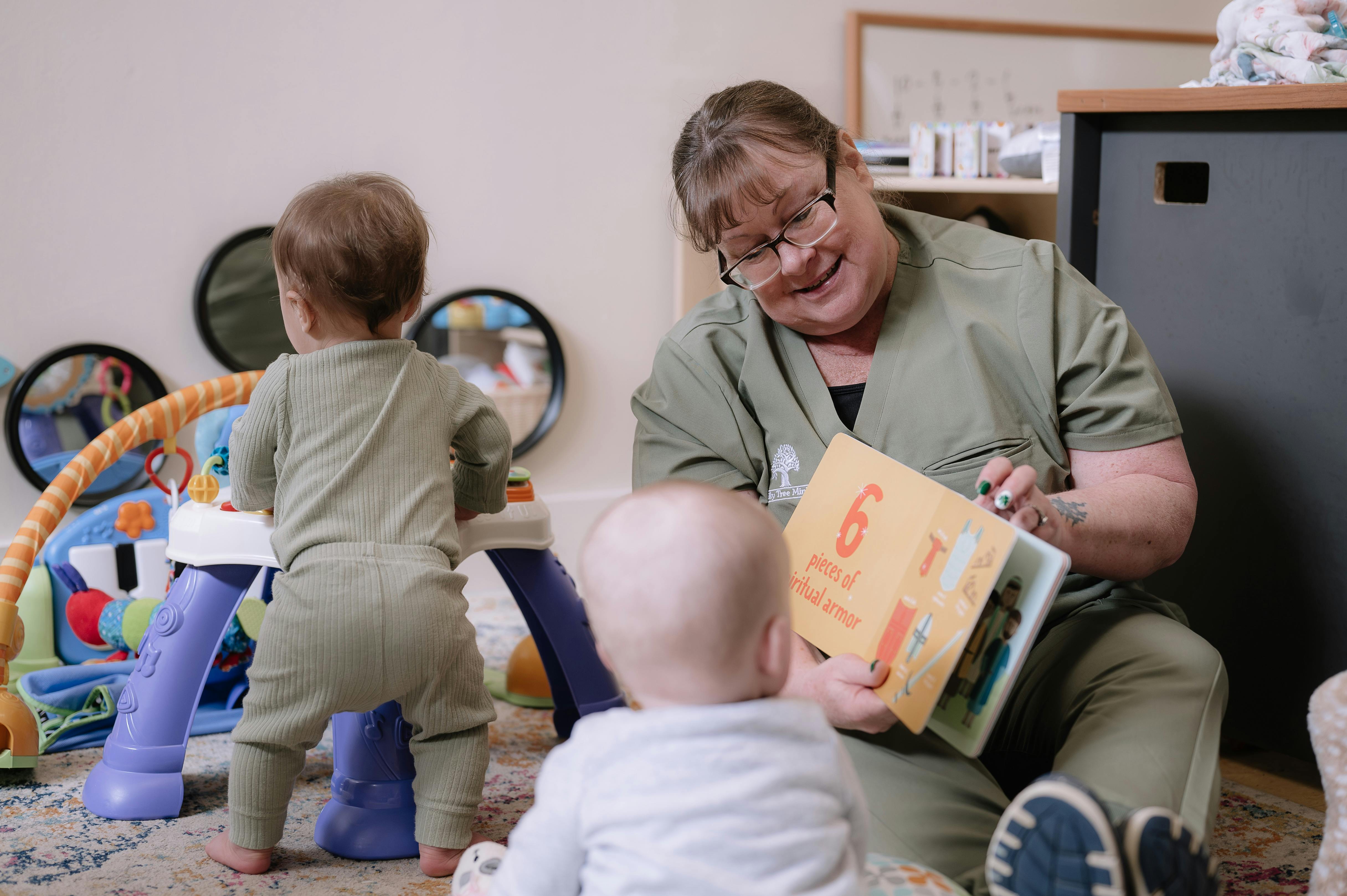 Adult reading a book to two children in a play area