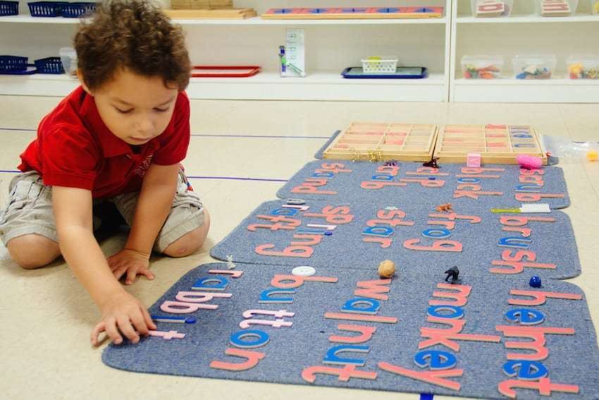 Child kneeling on floor, placing letters on a word mat