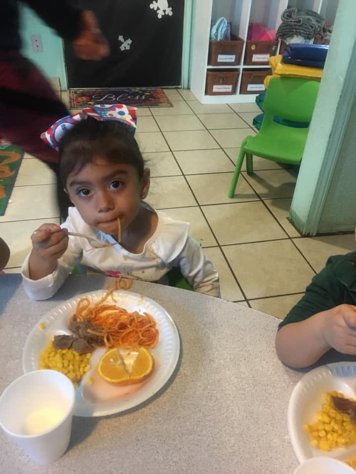 Child eating spaghetti from a plate at a table