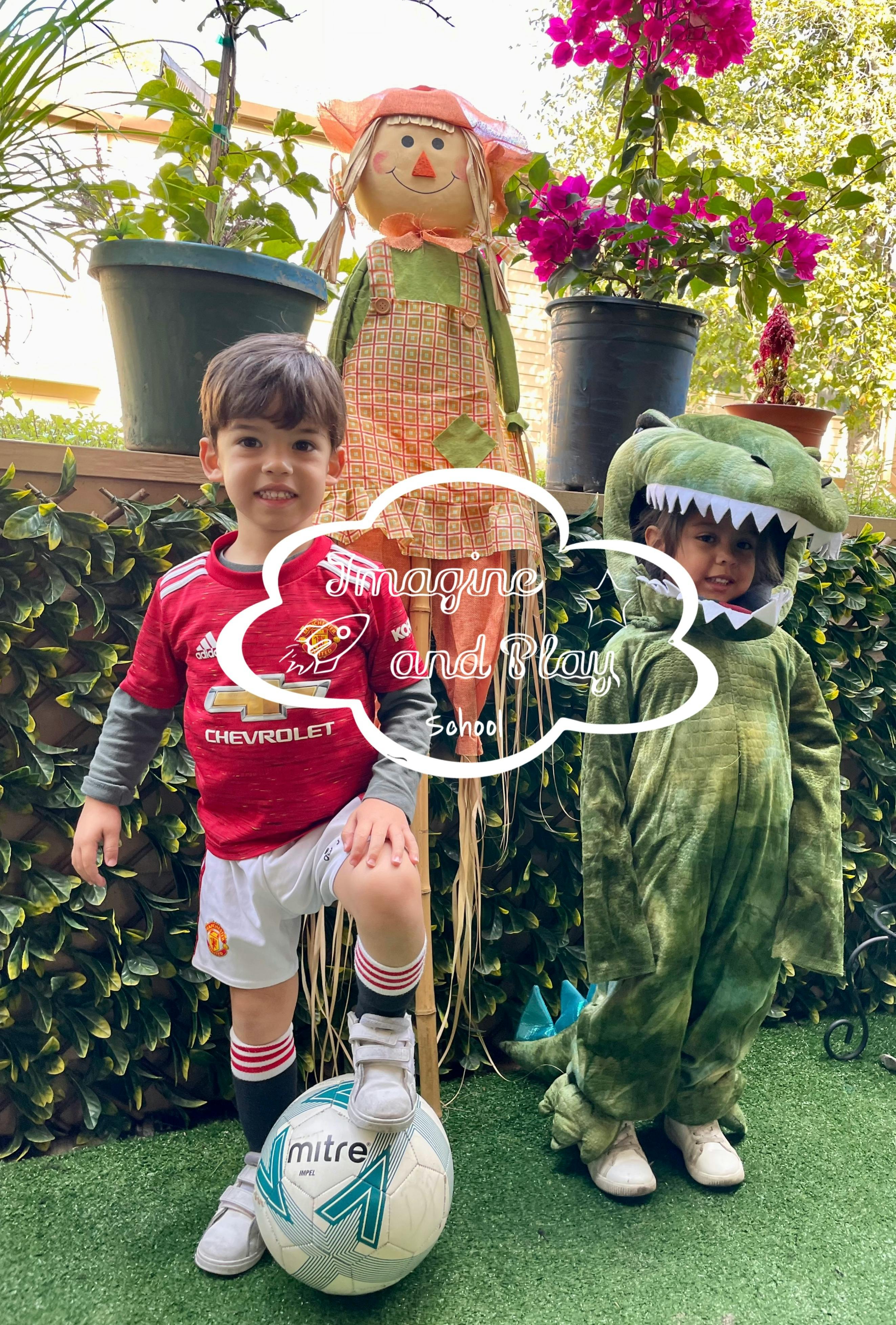 Child in a red soccer jersey with one foot on a ball, child in a green dinosaur costume