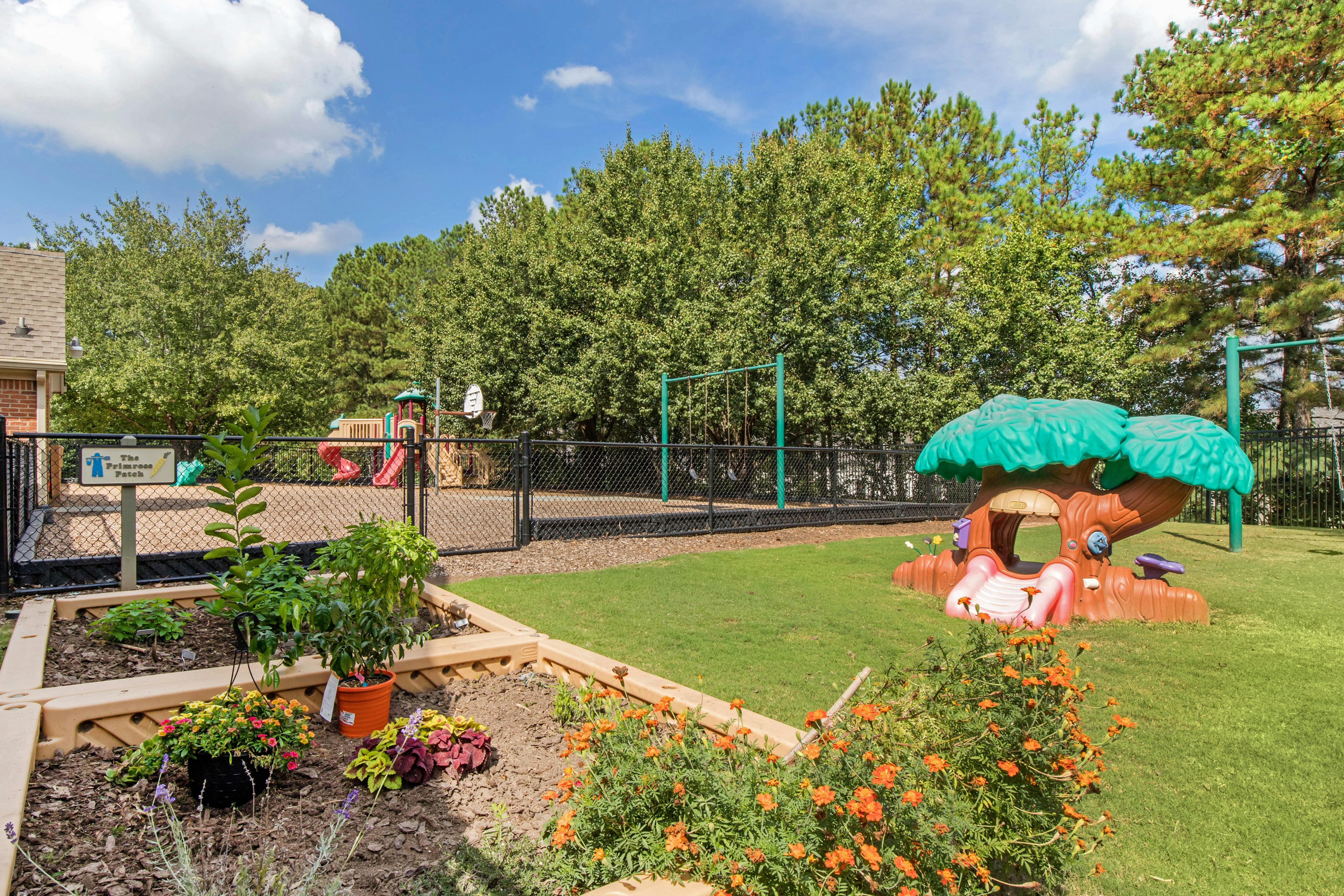 A fenced playground with slides and swings, next to a garden