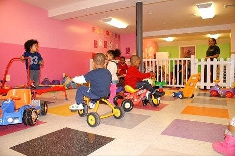 Children playing on tricycles and toy cars in a brightly colored room