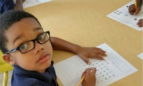 Child in glasses writing on a worksheet at a table