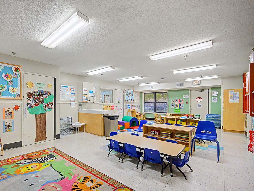 Classroom with small tables and chairs, colorful rug, and bulletin board