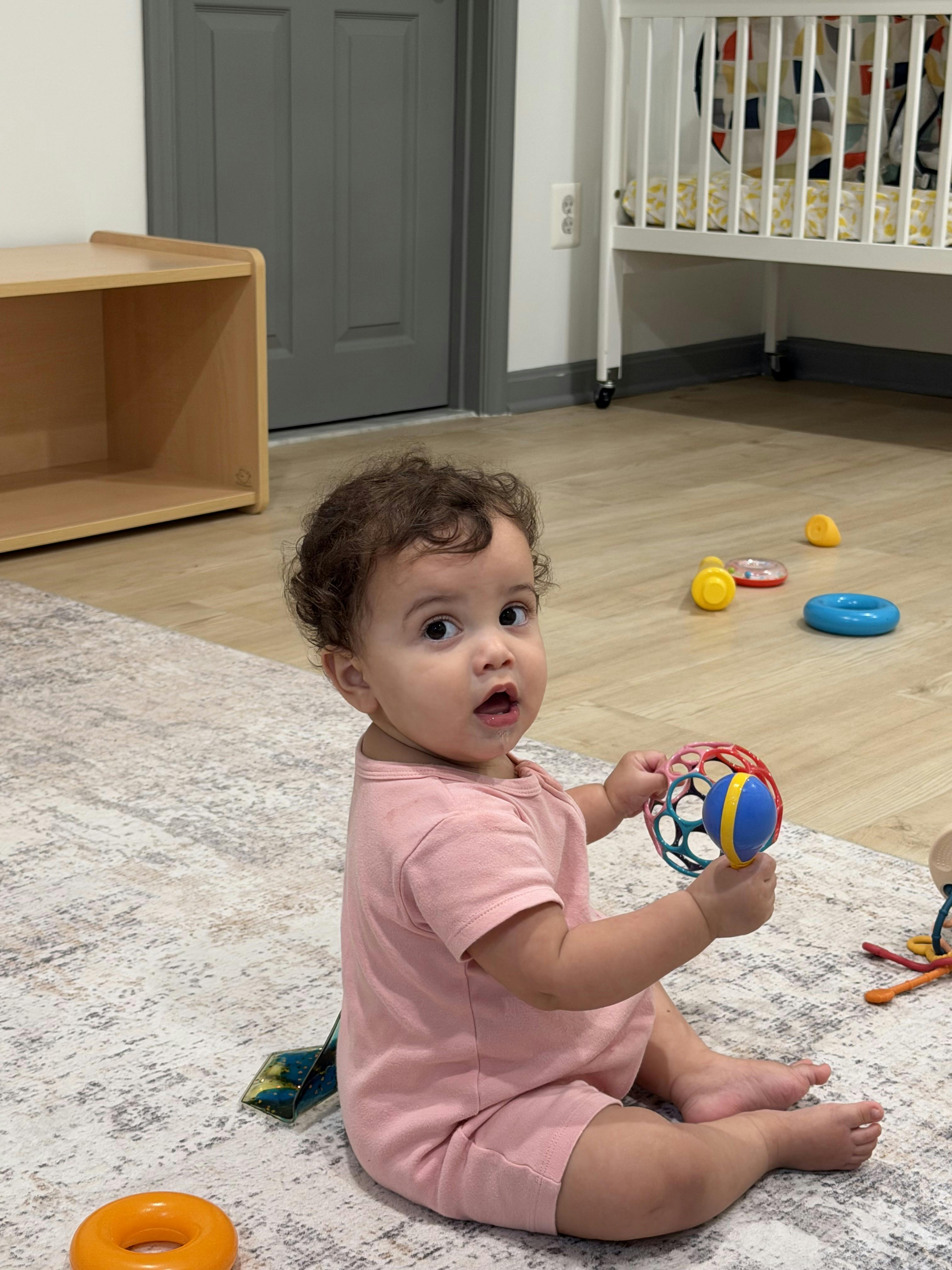 Child sitting on a rug holding a toy ball