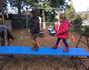 Two children walking on a blue balance beam on a playground