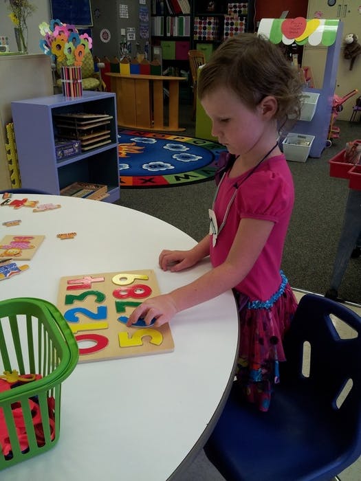 Child playing with a number puzzle at a table in a classroom