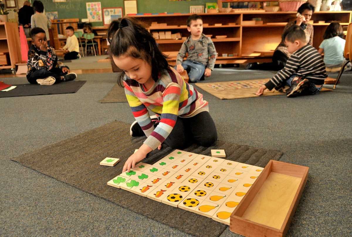 Child playing with a wooden puzzle on a mat in a classroom