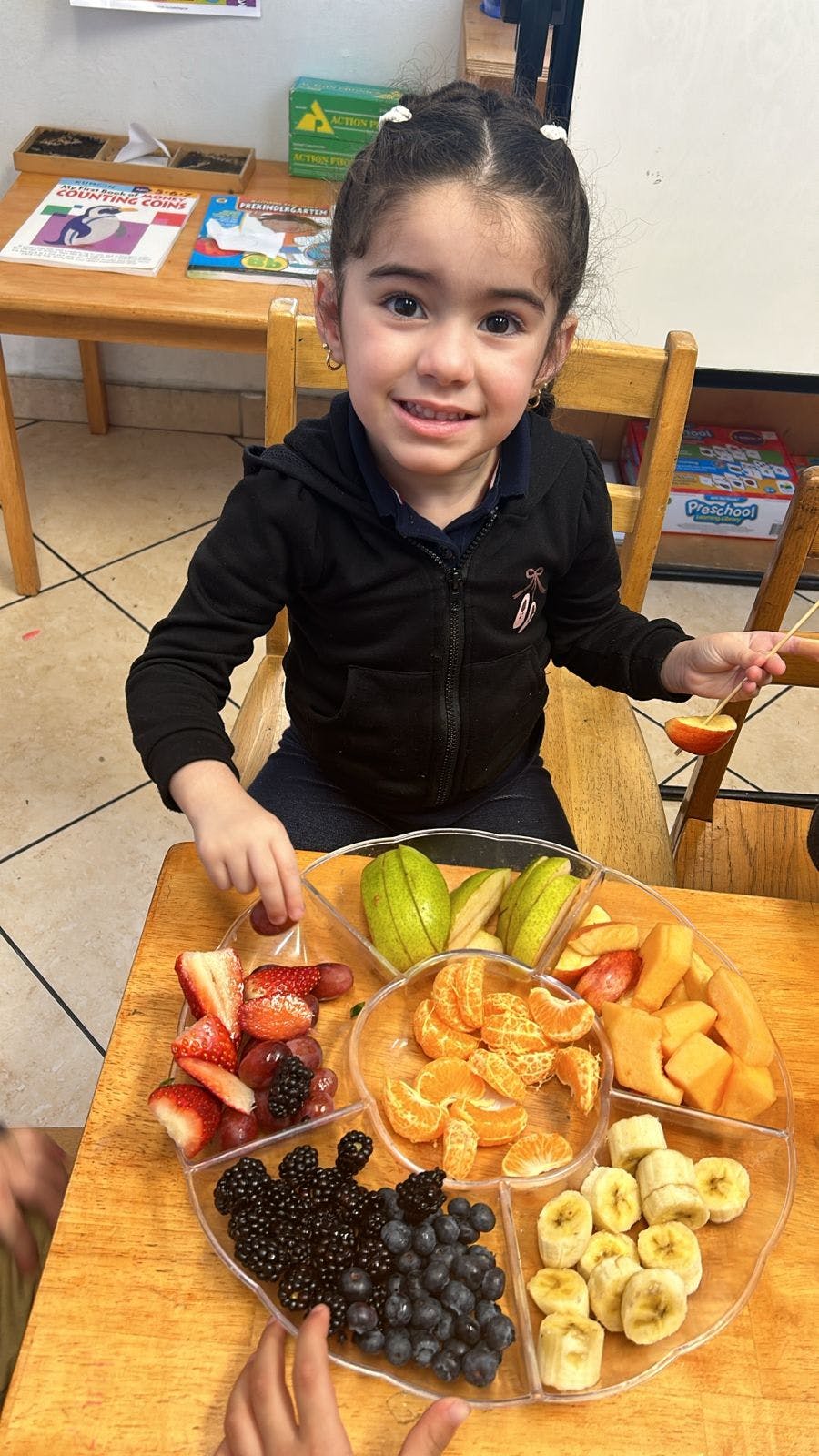 Child sitting at a desk with a tray of fresh fruit