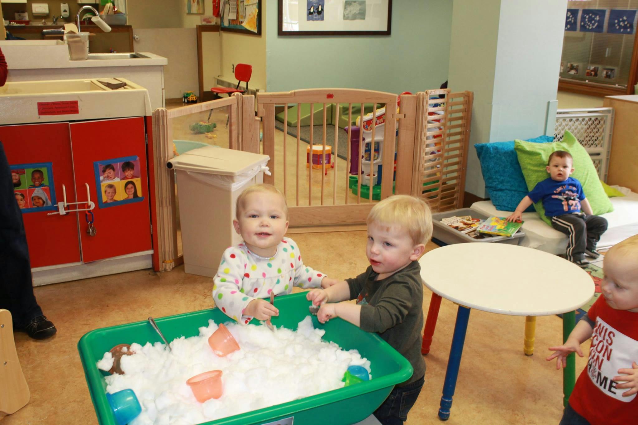 Three children playing with a sensory bin filled with white material