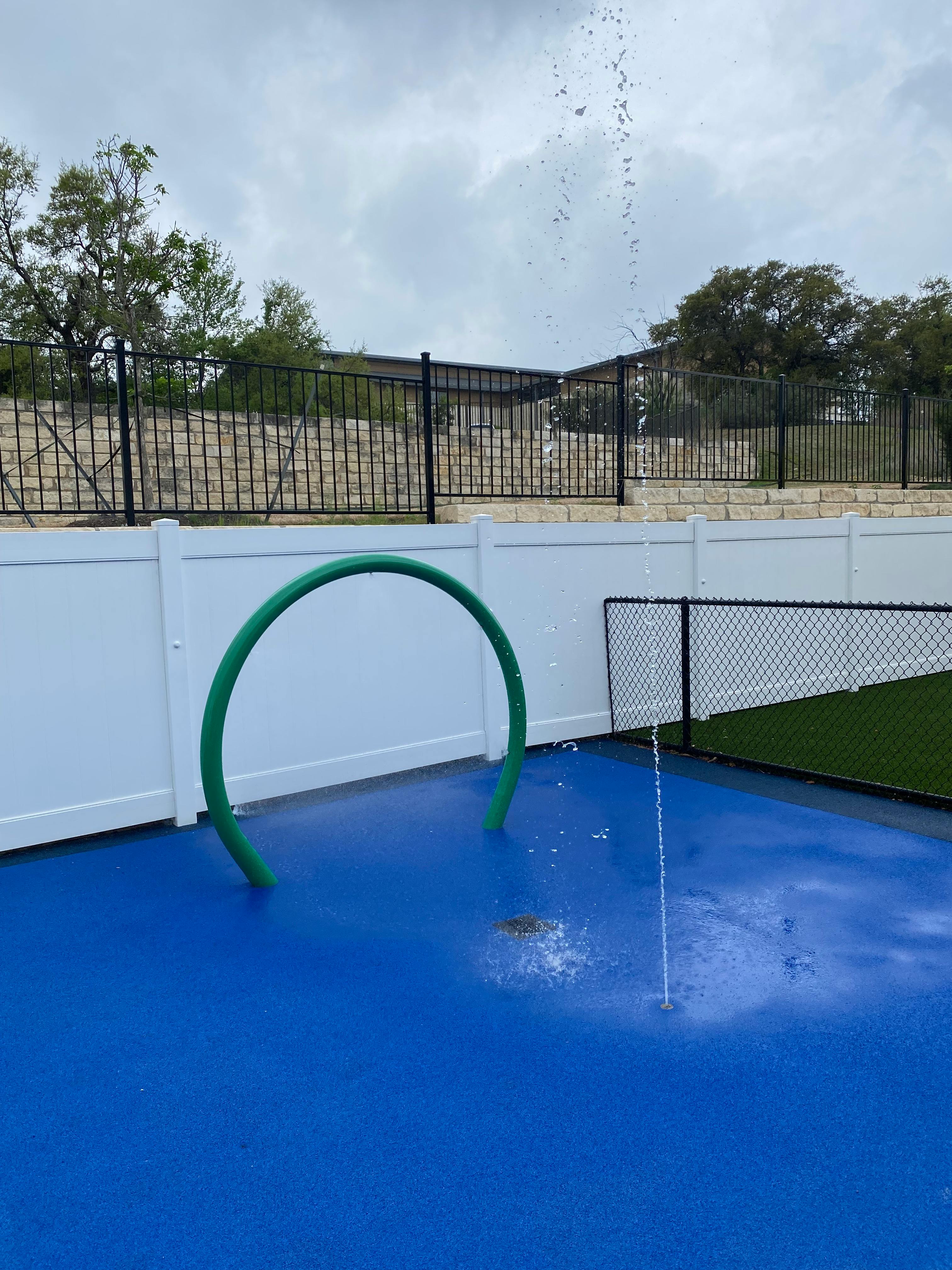 Water spraying from a blue splash pad with a green arch