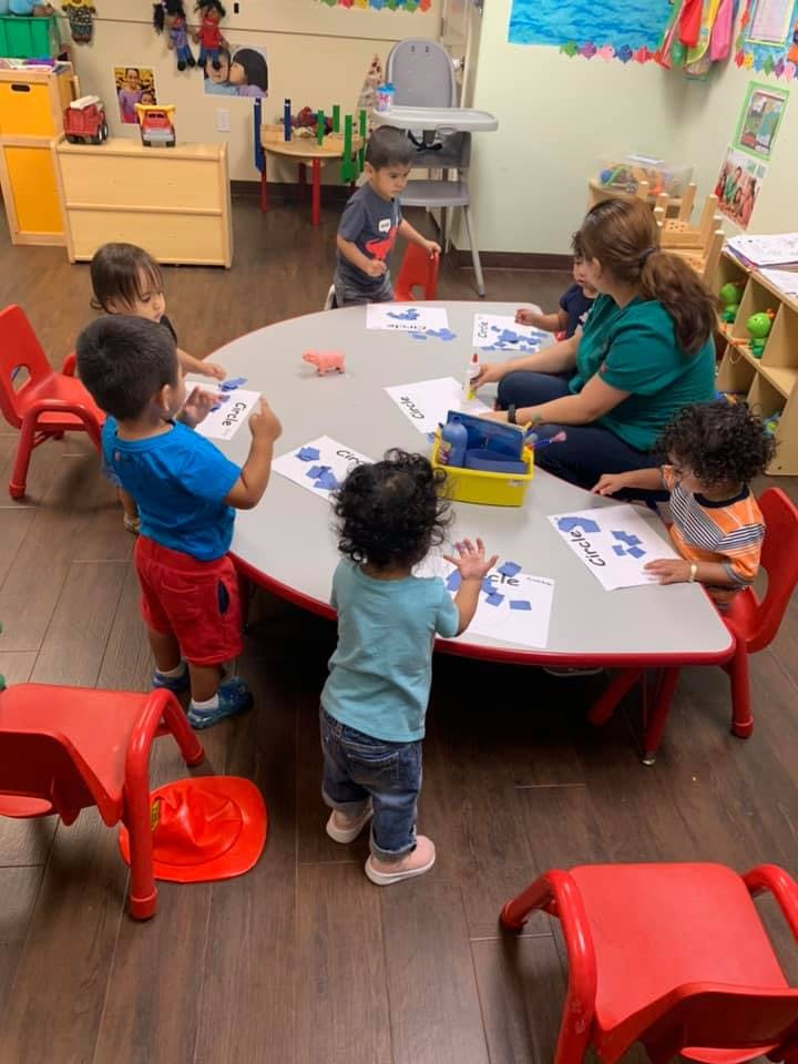Adult and children at a table with papers and shapes in a classroom