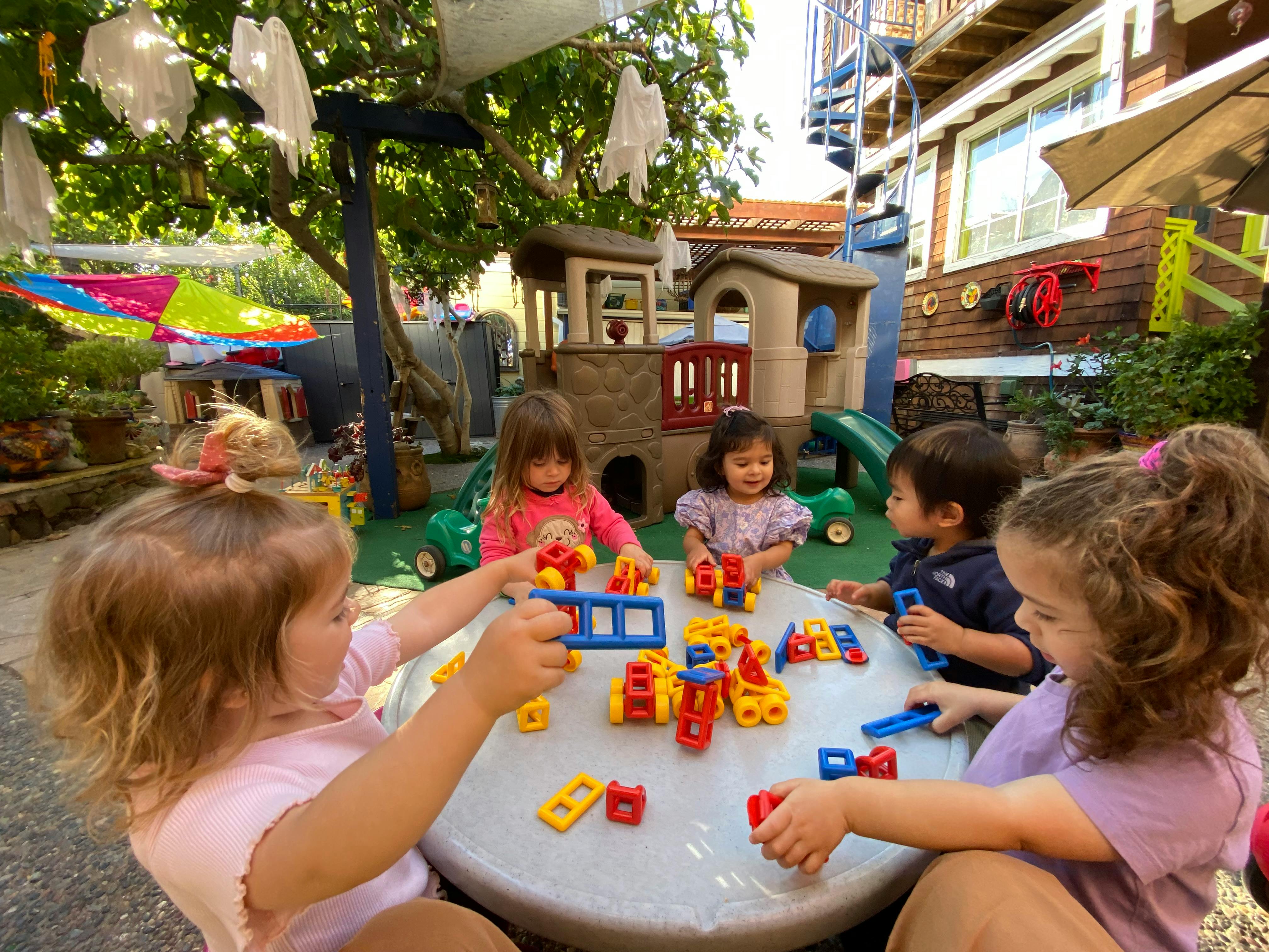 Children playing with building blocks at a table outdoors