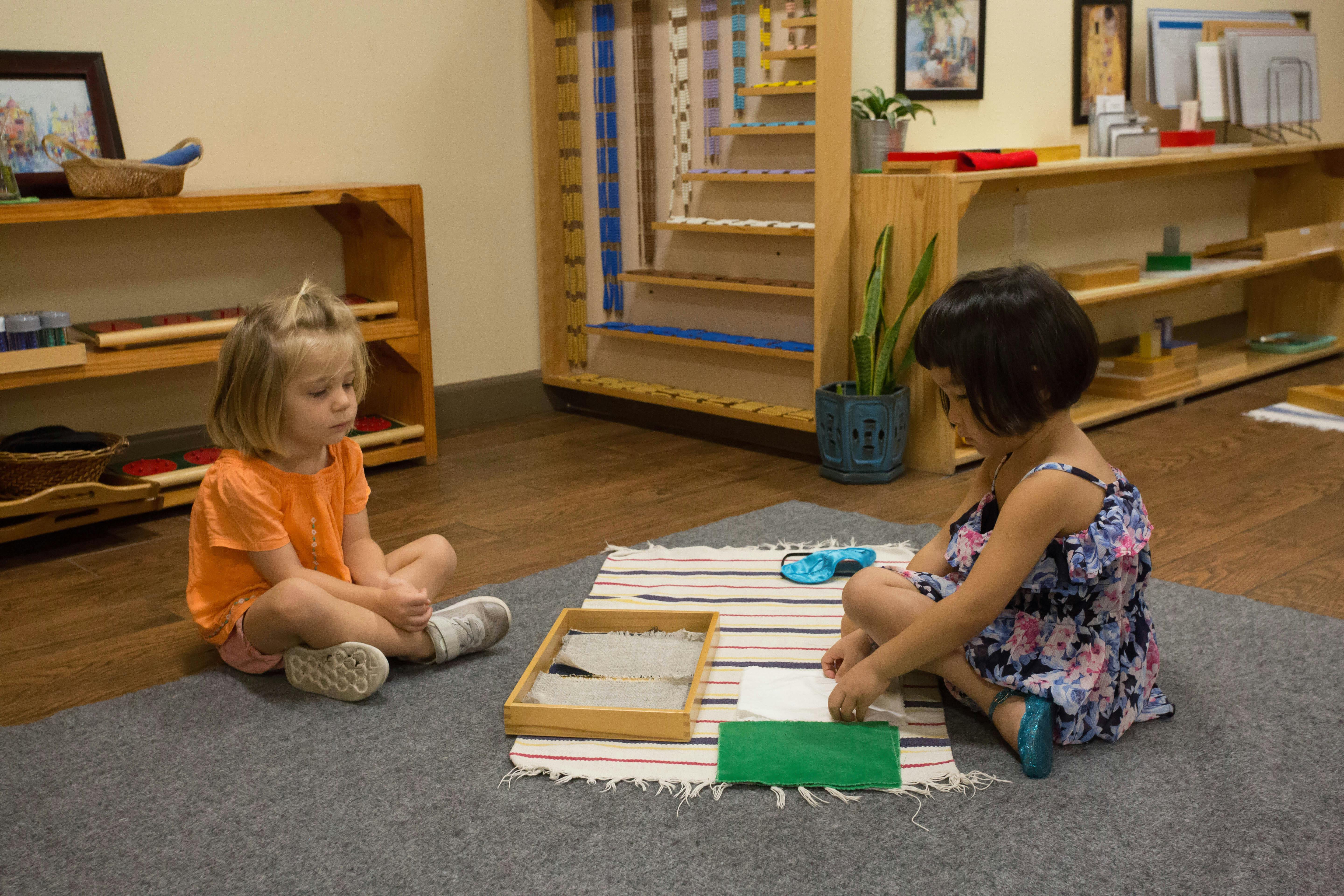 Two children sitting on a rug with a tray and learning materials