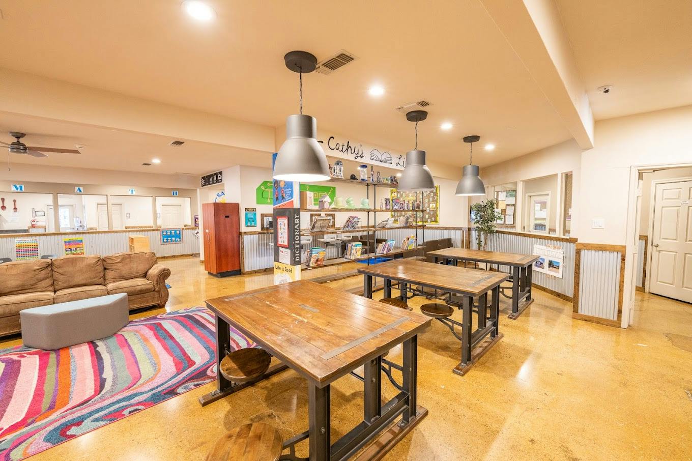 Library room with wooden tables, a brown couch, and colorful patterned rug