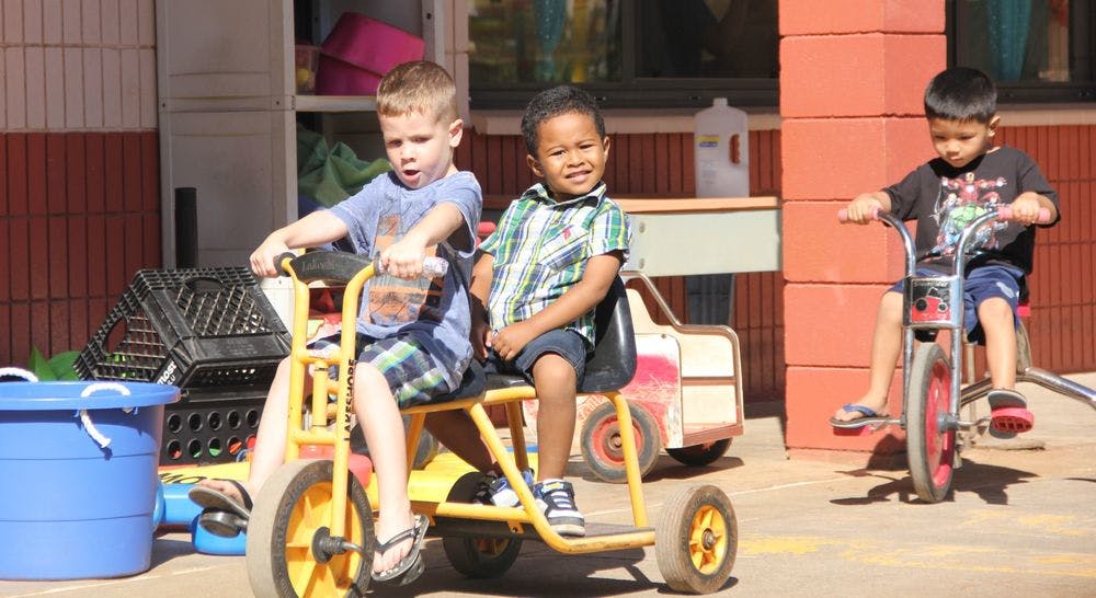 Three children riding tricycles outdoors