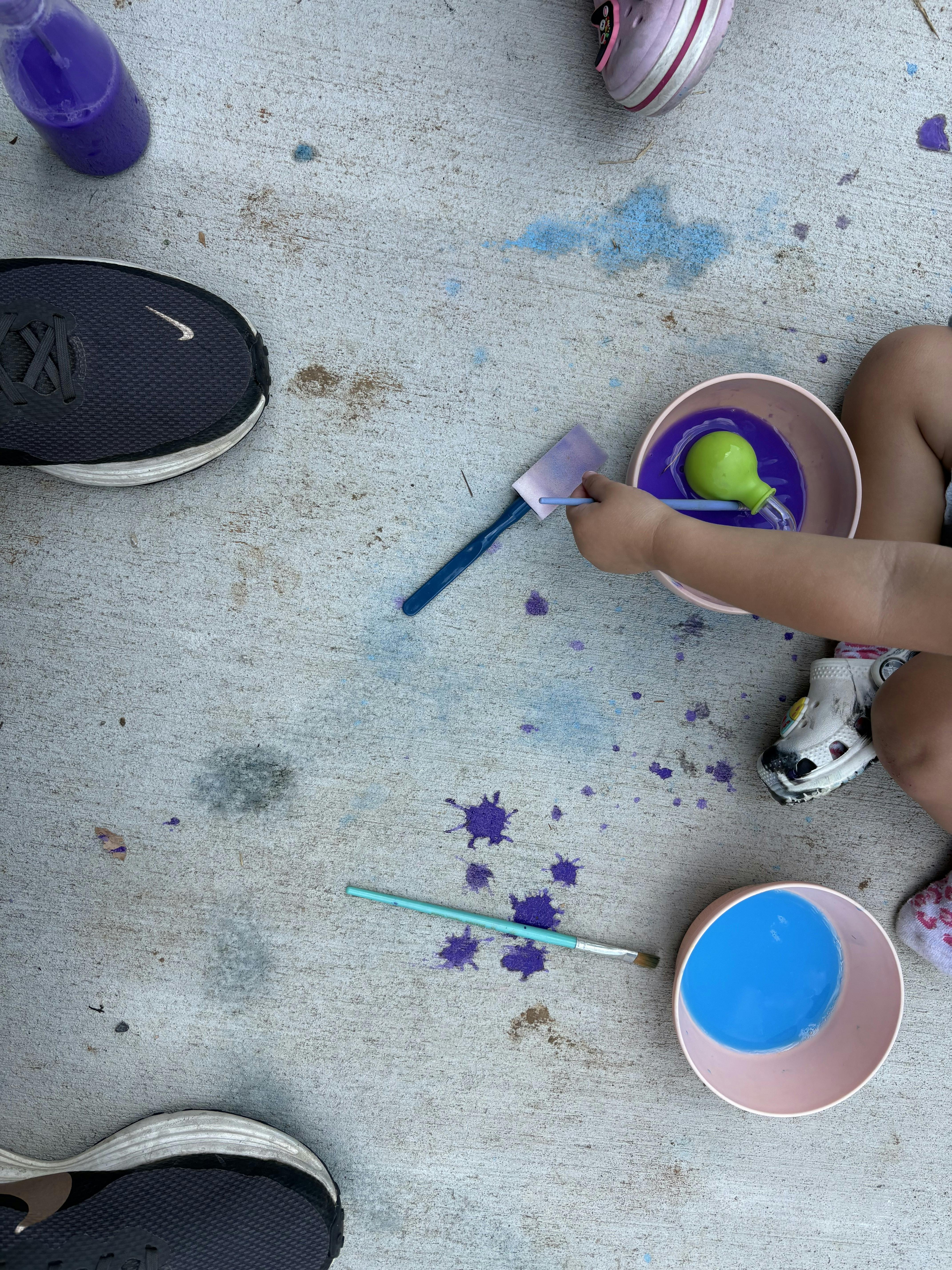 Child sitting on concrete painting with brushes and colored liquids