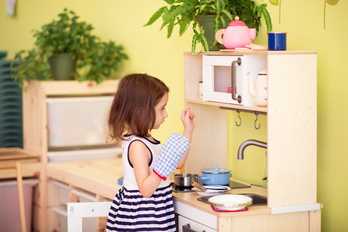 Child wearing an oven mitt playing with a toy kitchen set